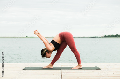 young girl doing yoga outdoors on the pier by the lake.