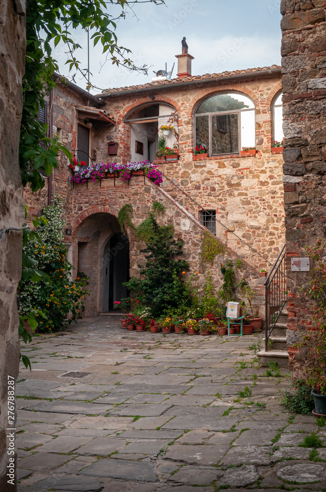 Montemerano, Grosseto, Tuscany. Public square of the medieval town. Stone paving and red brick walls. Arch with stairs adorned with flowers