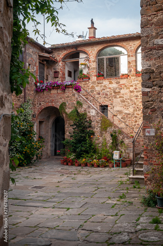 Montemerano  Grosseto  Tuscany. Public square of the medieval town. Stone paving and red brick walls. Arch with stairs adorned with flowers