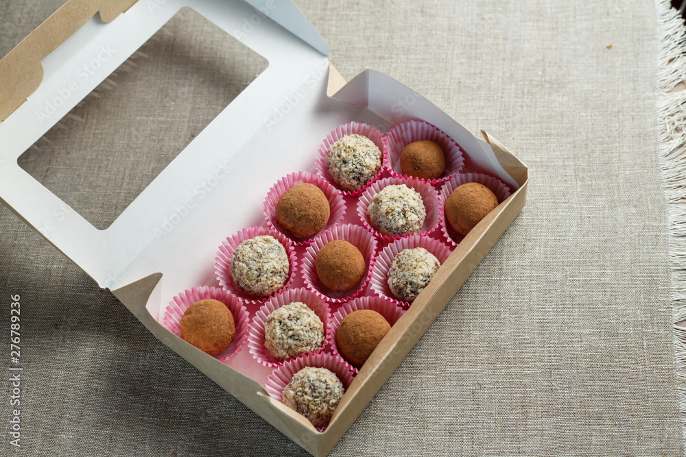Obraz premium Homemade candy in the form of balls of dried fruit with walnut and cocoa powder in the box on a linen napkin on the table. Healthy food without sugar and gluten.