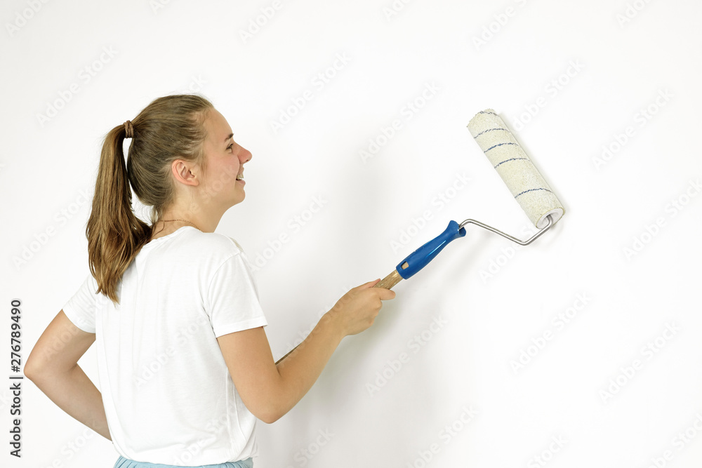 A young girl makes repairs: paints the walls with white paint using a roller. A young girl makes repairs: paints the walls with white paint using a roller.