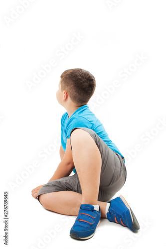 Portrait of a cute boy sitting on the floor, looking up on wall. Isolated on white background