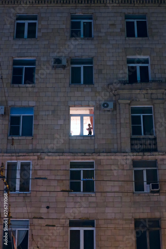 silhouette of a child in the illuminated window of an apartment building in the evening
