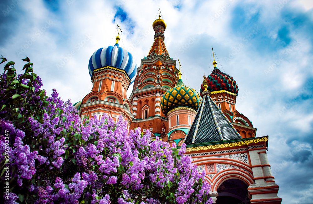 Spring in Moscow Red Square. A vibrant purple lilac tree blossom and a famous Saint Basil's Cathedral with blue cloudy sky at the backround.  - obrazy, fototapety, plakaty 