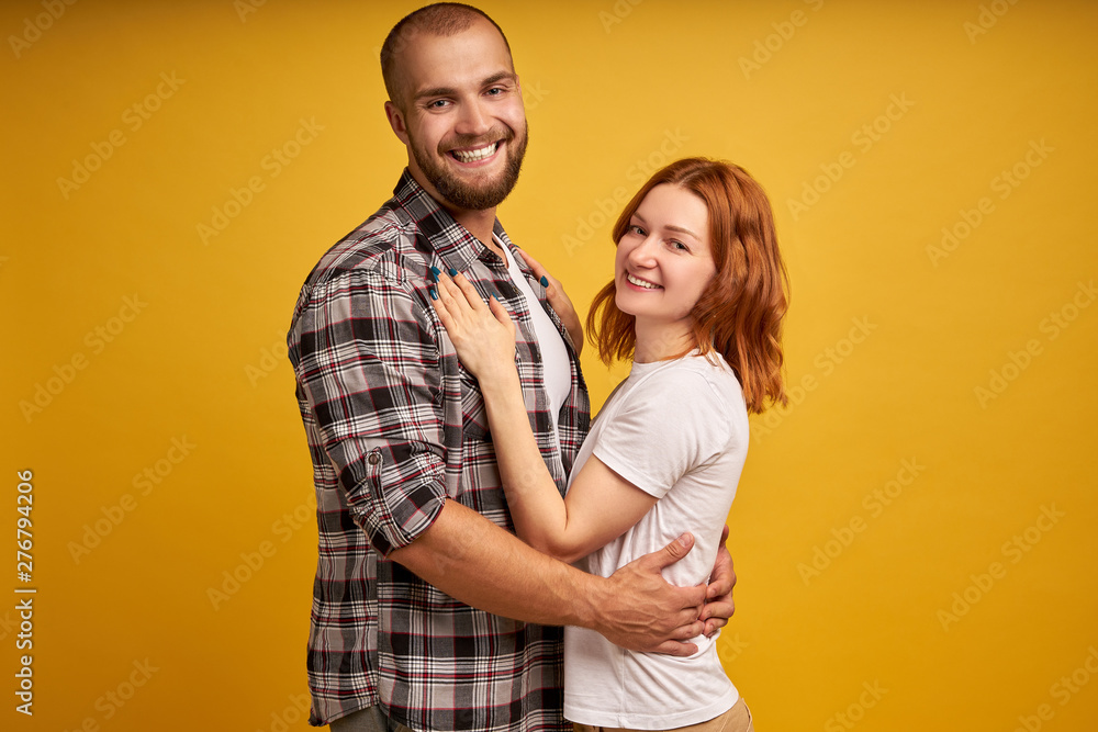 Photo of cheerful lovely family coupe cuddle each other, have fun together, look with big love and affection, wear stylish clothes, isolated over yellow background. People and closeness concept Photo of cheerful lovely family coupe cuddle each other, have fun together, look with big love and affection, wear stylish clothes, isolated over yellow background. People and closeness concept
