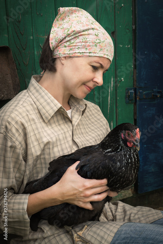 woman farmer in men's clothing, holding a black chicken in her hands in the rural scene