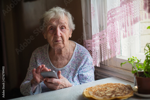 An old woman sits with a smartphone in her hands.