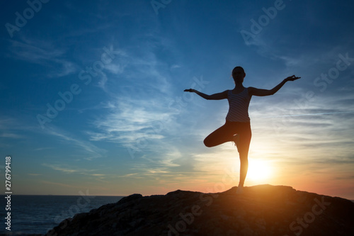 Woman yoga silhouette, performs concentration exercises during sunset on the sea coast.