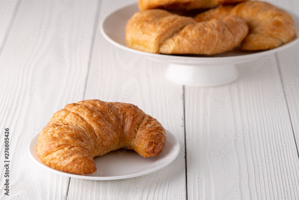 Warm crispy flaky croissant roll on white plate and distressed table. Warm crispy flaky croissant roll on white plate and distressed table.