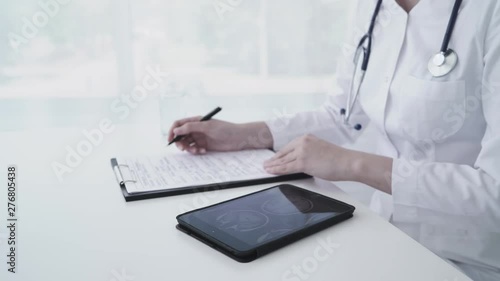 Wallpaper Mural Female caucasian doctor using tablet and writing diagnosis in medical form and documents. Close up 4K Torontodigital.ca
