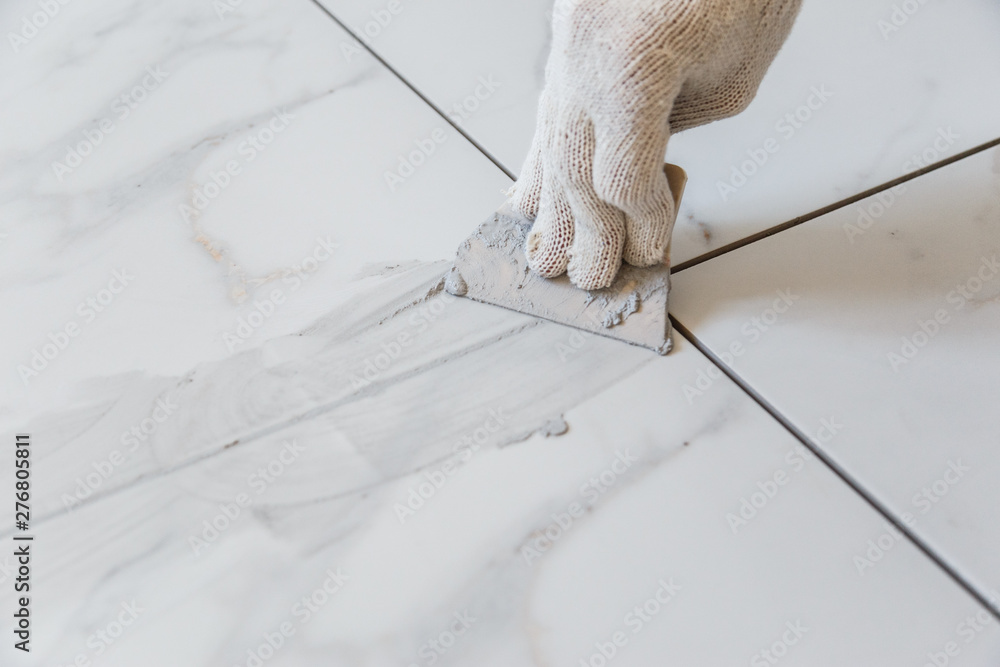 Grouting tiles seams with a rubber trowel.