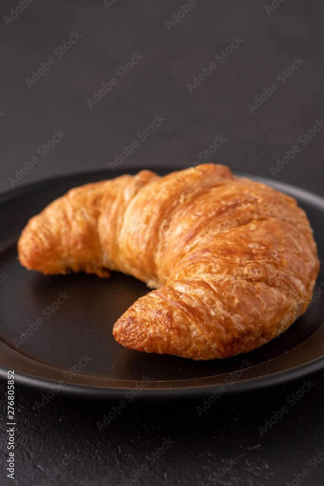 Warm crispy flaky croissant roll on white plate and distressed table.