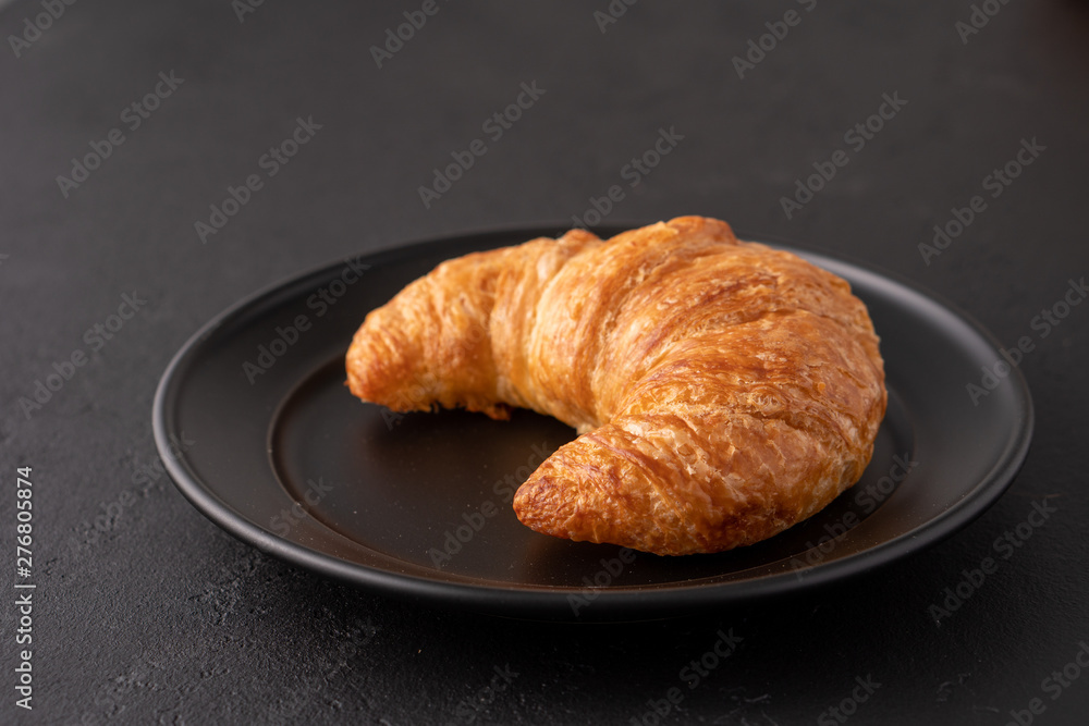 Warm crispy flaky croissant roll on white plate and distressed table.