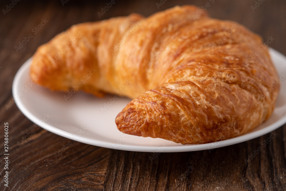 Warm crispy flaky croissant roll on white plate and distressed table.