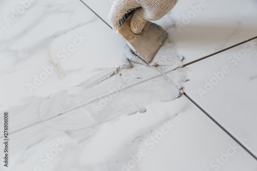 Grouting tiles seams with a rubber trowel.