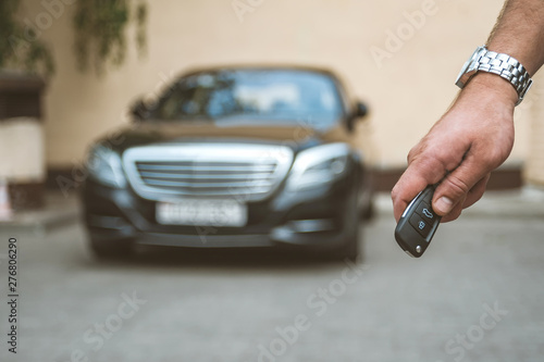 The man opens the car with a keychain, in the background is a black car and a yellow background.