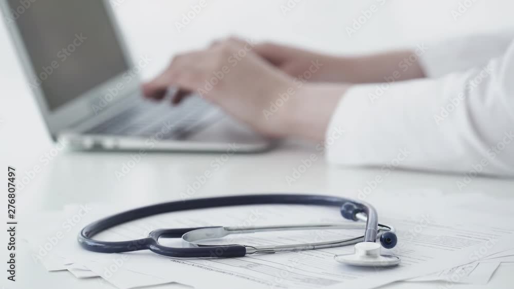 Doctor is typing text on laptop, stethoscope on medical documents Doctor is typing text on laptop, stethoscope on medical documents