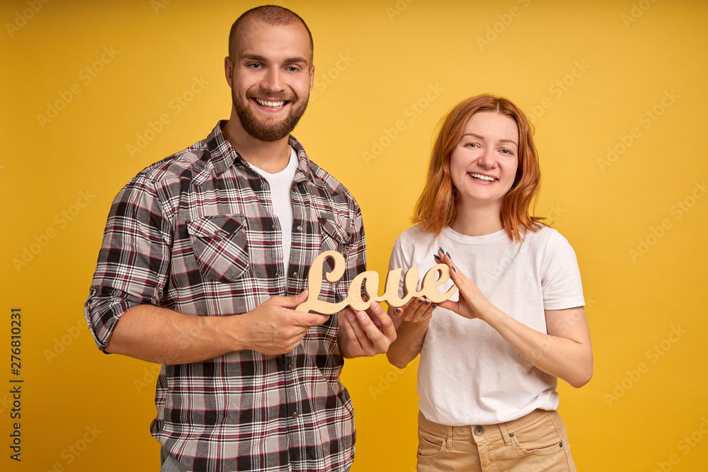 Portrait of charming charismatic man and woman holding a wooden statuette of the word Love. isolated over yellow background Portrait of charming charismatic man and woman holding a wooden statuette of the word Love. isolated over yellow background