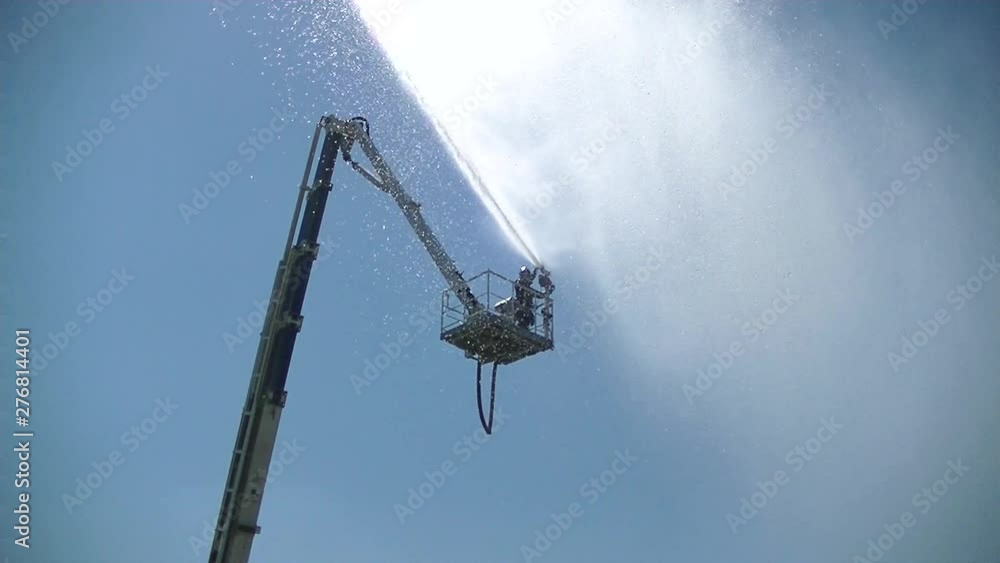 Fireman from a tower directs a stream of water into the chamber from a fire pump - water cannon. Large drops fall in the shower. Sun glare. Slow motion. Fireman from a tower directs a stream of water into the chamber from a fire pump - water cannon. Large drops fall in the shower. Sun glare. Slow motion.