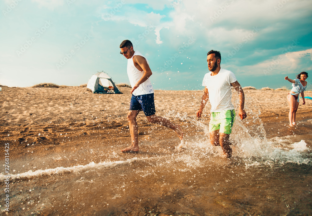 Fototapeta premium Friends running through the water at sunset