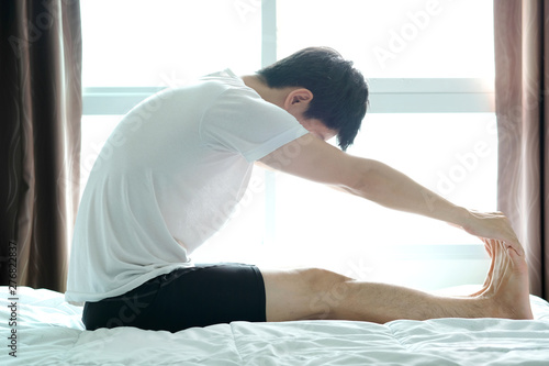 Man stretches muscles and playing yoga on the bed in the bedroom in the morning.