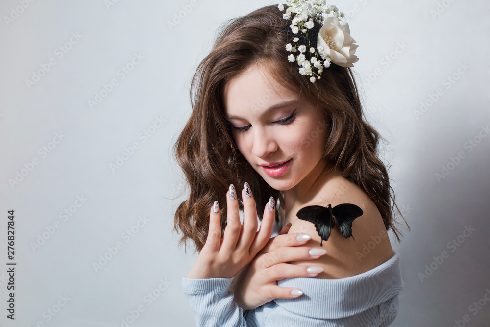 A beautiful young girl with dark curls shows two palms with a gentle manicure and looks at a black bow tie on her shoulder, smiles sweetly at her. Copyspace.