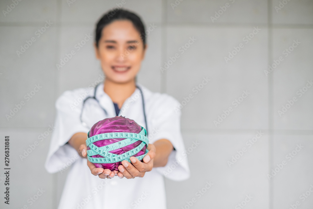 Smiling Asian woman doctor in medical white gown holding a purple cabbage wrap with measuring tape. Health concept. Smiling Asian woman doctor in medical white gown holding a purple cabbage wrap with measuring tape. Health concept.