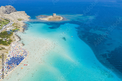 Stunning aerial view of the Spiaggia Della Pelosa (Pelosa Beach) full of colored beach umbrellas and people sunbathing and swimming in a beautiful turquoise clear water. Stintino, Sardinia, Italy. © Travel Wild
