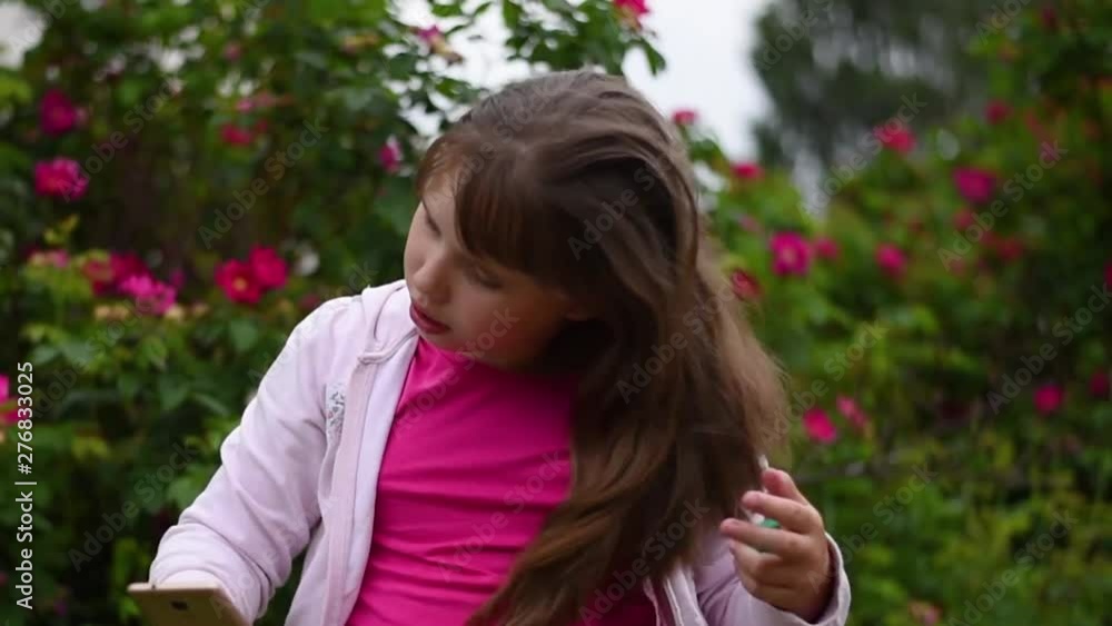 European girl with blonde hair taking pictures of herself on her smartphone. girl takes a selfie on the phone in the garden on a background of blooming roses European girl with blonde hair taking pictures of herself on her smartphone. girl takes a selfie on the phone in the garden on a background of blooming roses
