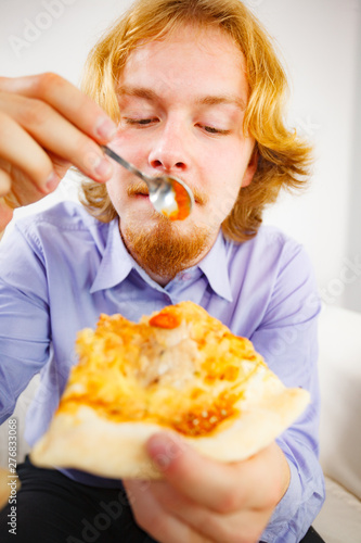 Man eating pizza adding tomato sauce