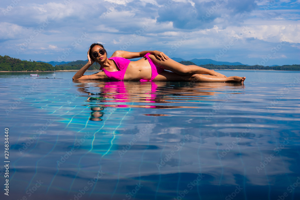 Along Side Pool with adult Mix Race Tanned Skinny Woman in sexy sensual pink bikini Swimsuit take vacation holiday in Summer Island and fashion posing over blue Sky Cloud, copy space for text logo Along Side Pool with adult Mix Race Tanned Skinny Woman in sexy sensual pink bikini Swimsuit take vacation holiday in Summer Island and fashion posing over blue Sky Cloud, copy space for text logo