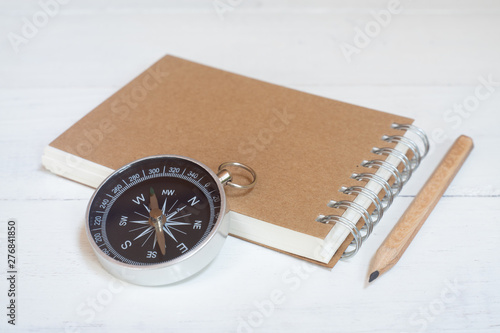 Compass and brown notebook on white wooden table background, journey planning concept