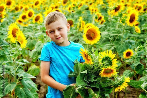 Portrait of a little boy with a bouquet of flowers of sunflower in the field .