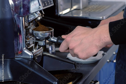 Barista grinding coffee beans using coffee machine and holder.