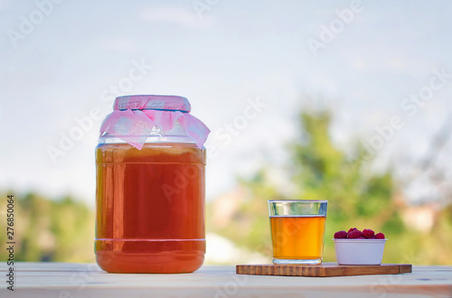 Kombucha in a jar on a light wooden table against the sky, a glass filled with Kombucha with raspberries.