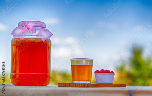 Kombucha in a jar on a light wooden table against the sky, a glass filled with Kombucha with raspberries.