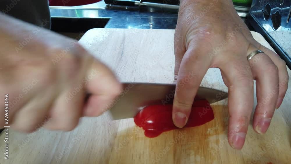 A man dices red peppers on a wooden chopping board at home. A man dices red peppers on a wooden chopping board at home.