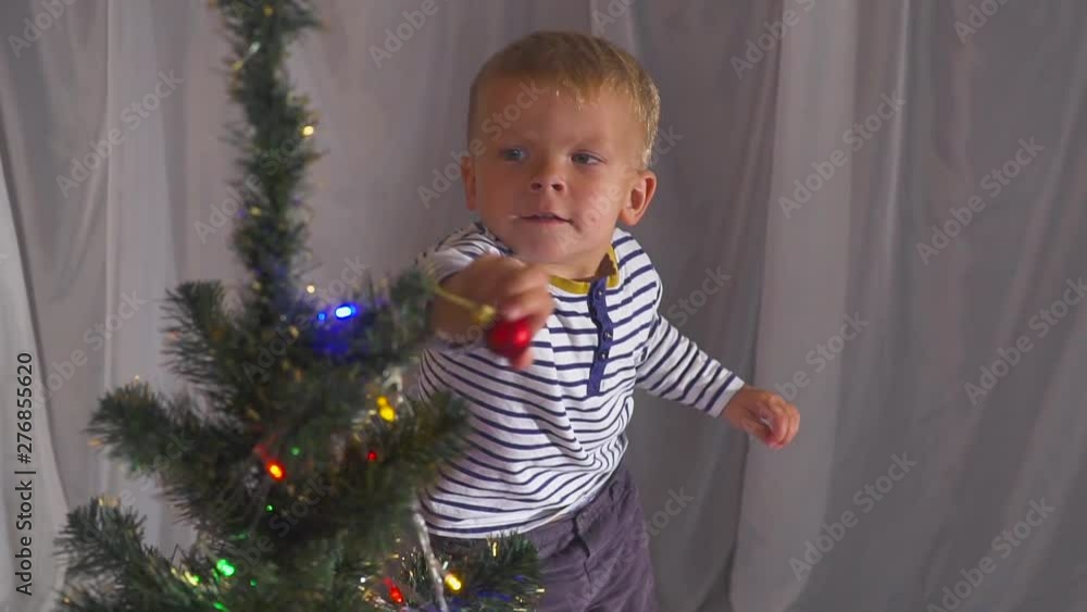 two year old boy playing with Christmas toys on Christmas tree, close up. Portrait of a child near a Christmas tree. two year old boy playing with Christmas toys on Christmas tree, close up. Portrait of a child near a Christmas tree.