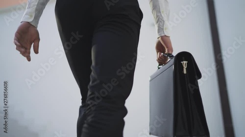 Businessman with briefcase walking across the office building. Close up. 4K photo