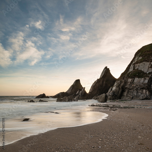 Stunning sunset landscape image of Westcombe Beach in Devon England with jagged rocks on beach and stunning cloud formations