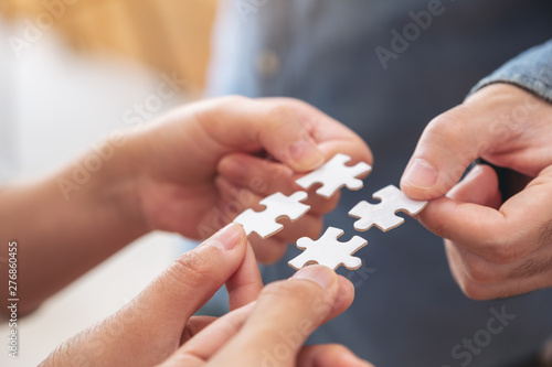 Closeup image of people's hands holding and putting a piece of white jigsaw puzzle together