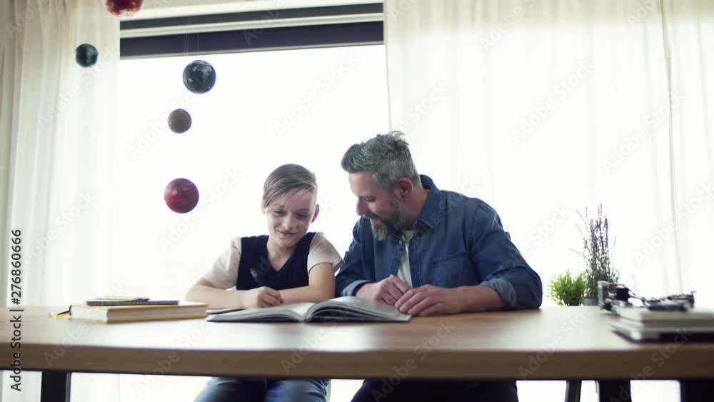 Mature father with small son sitting at table indoors, working on school project. Mature father with small son sitting at table indoors, working on school project.