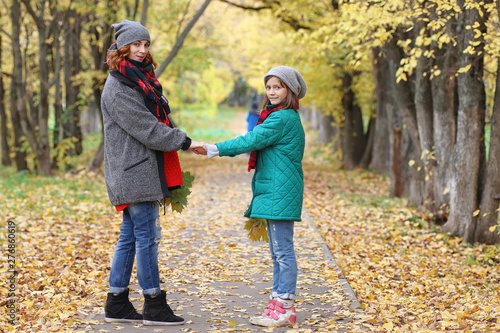 Young beautiful mother with her daughter on nature. A girl in a hat walks in the park. Girl in autumn city park in leaf fall.