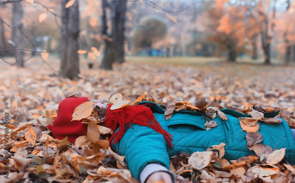 Obraz premium Girl in autumn city park in leaf fall. Young beautiful mother with her daughter on nature. A girl in a hat walks in the park.