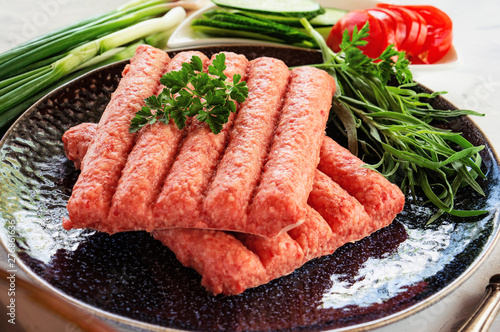 Chevapchichi is a national Balkan dish. Close up a row of fresh raw beef kebabs.