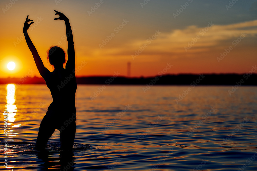 Silhouette of a ballerina dancing in the water in the setting sun.