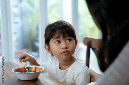 portrait of Little asian girl eating cereal for breakfast with mom
