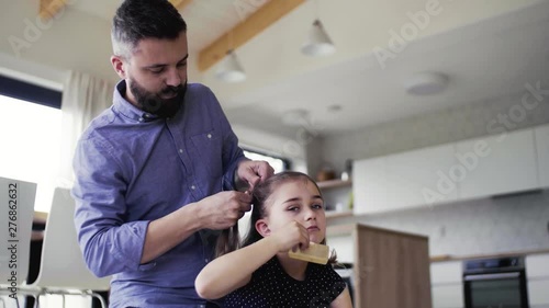 Mature father with small daughter indoors at home, plaiting hair.