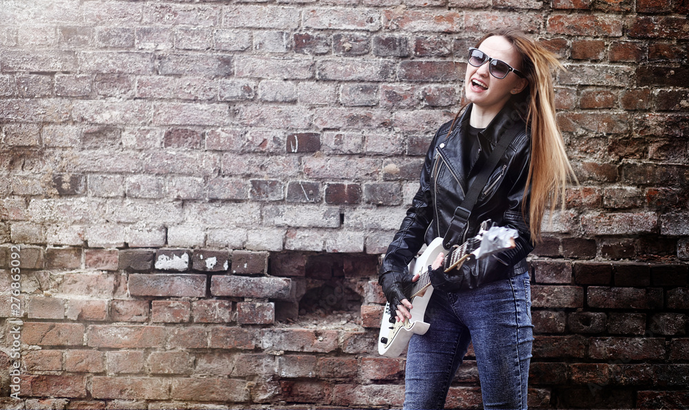 Beautiful young girl rocker with electric guitar. A rock musician girl in a leather jacket with a guitar sings. A rock band soloist plays the guitar and screams into the microphone. Beautiful young girl rocker with electric guitar. A rock musician girl in a leather jacket with a guitar sings. A rock band soloist plays the guitar and screams into the microphone.