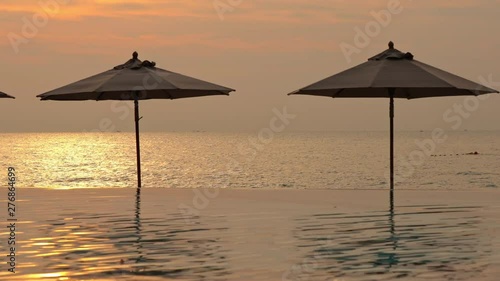 Pink orange yellow reflection in infinity pool and sea on sunset, Umbrellas. photo